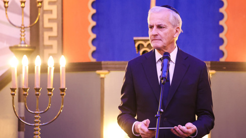 Støre står bak en mikrofon, holder talekort. Har en kippa (jødisk hodeplagg) på hodet.