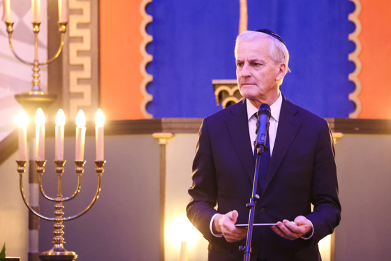 Støre står bak en mikrofon, holder talekort. Har en kippa (jødisk hodeplagg) på hodet.