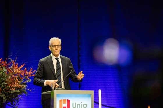 Statsministeren står bak en talerstol. Dresskledd. Gestikulerer i talen sin.