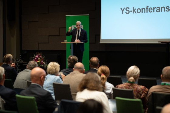 Støre står på en scene, snakker og ser utover deltakerne som sitter i salen.