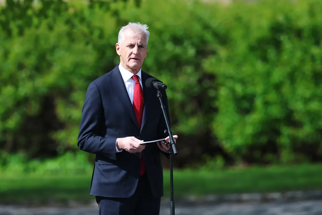 Statsministeren taler. Holder talerkortene sine og står bak en mikrofon.