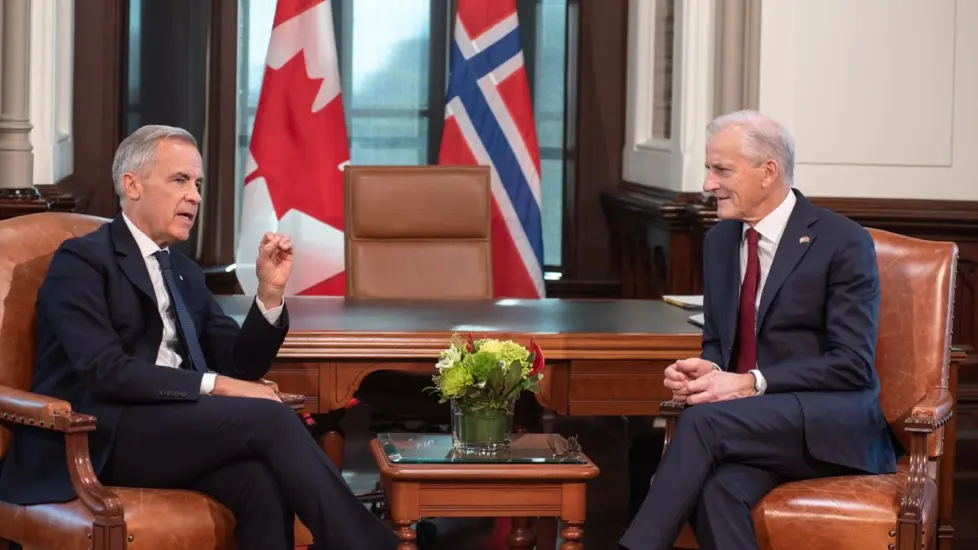 Mark Carney og Jonas Gahr Støre sitter i lenestoler foran kanadisk og norsk flagg.
