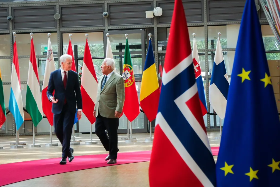 Støre og Costa går og prater sammen. Flagg i bakgrunnen og rundt dem.
