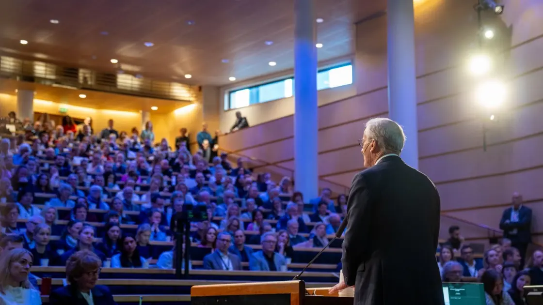 Statsministeren med ryggen til. Oversiktsbilde over publikum.