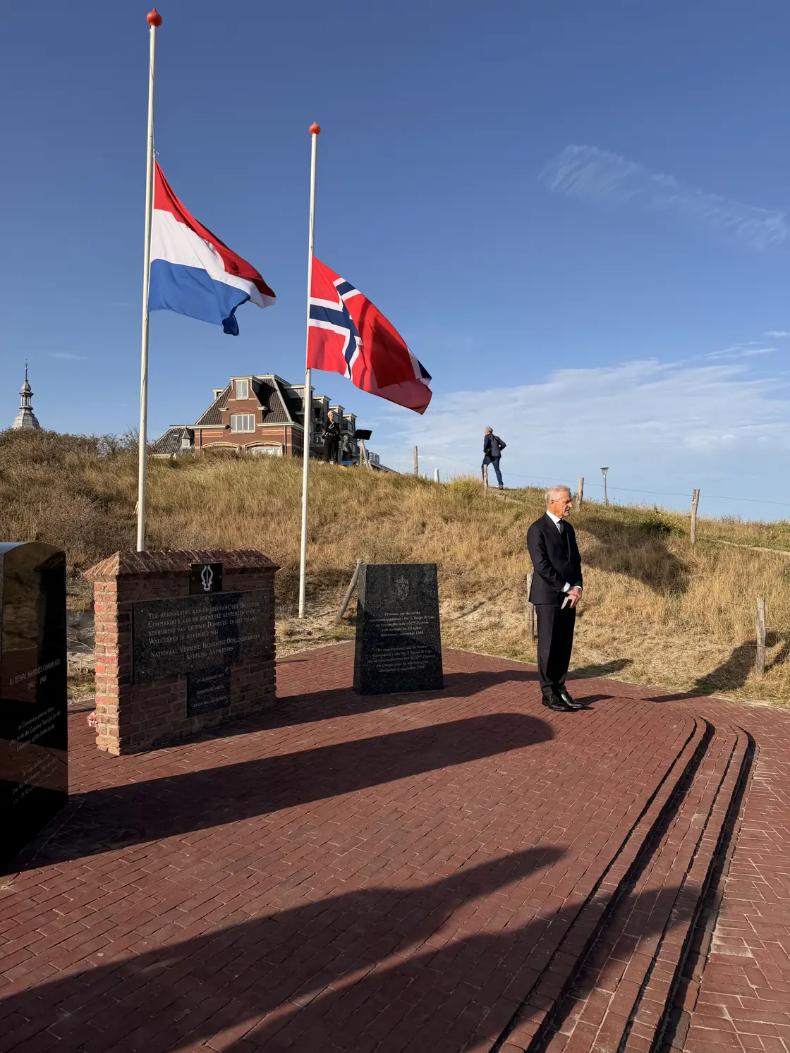 Statsministeren står foran minnestedet med nederlandsk og norsk flagg på halv stang.