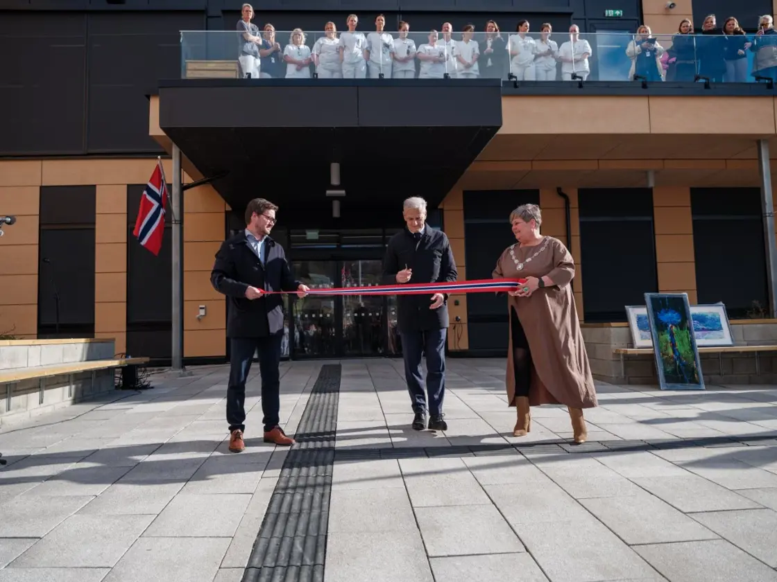 Statsministeren klipper over et bånd i norske farger for å markere åpningen av helsehuset.
