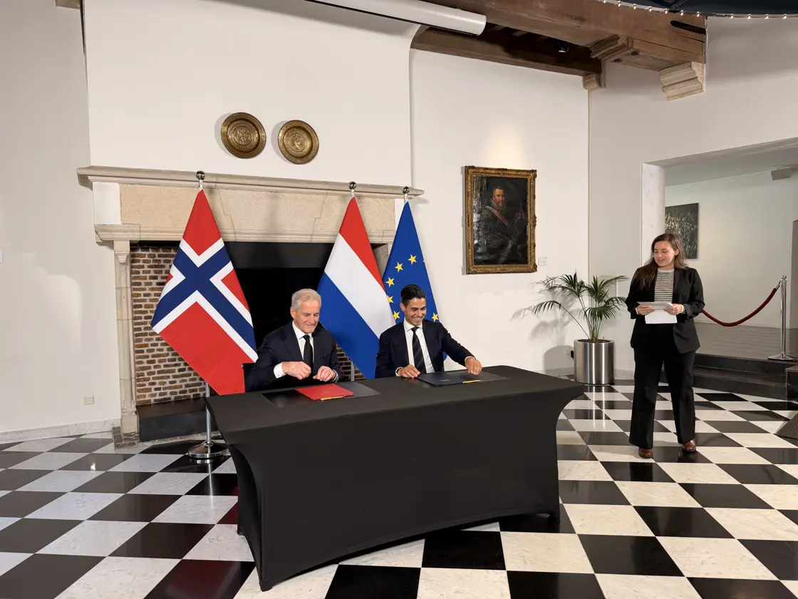 Støre og Jetten sitter bak et stort skrivebord med hver sin mappe med innhold som ligger klar for undertegning.