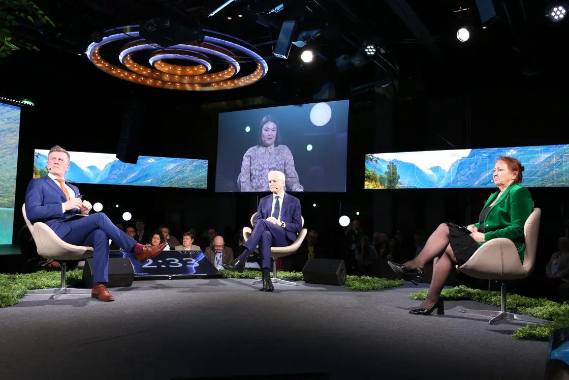 Samtale mellom tre på scenen. Det spilles av en video på en skjerm i bakgrunnen.