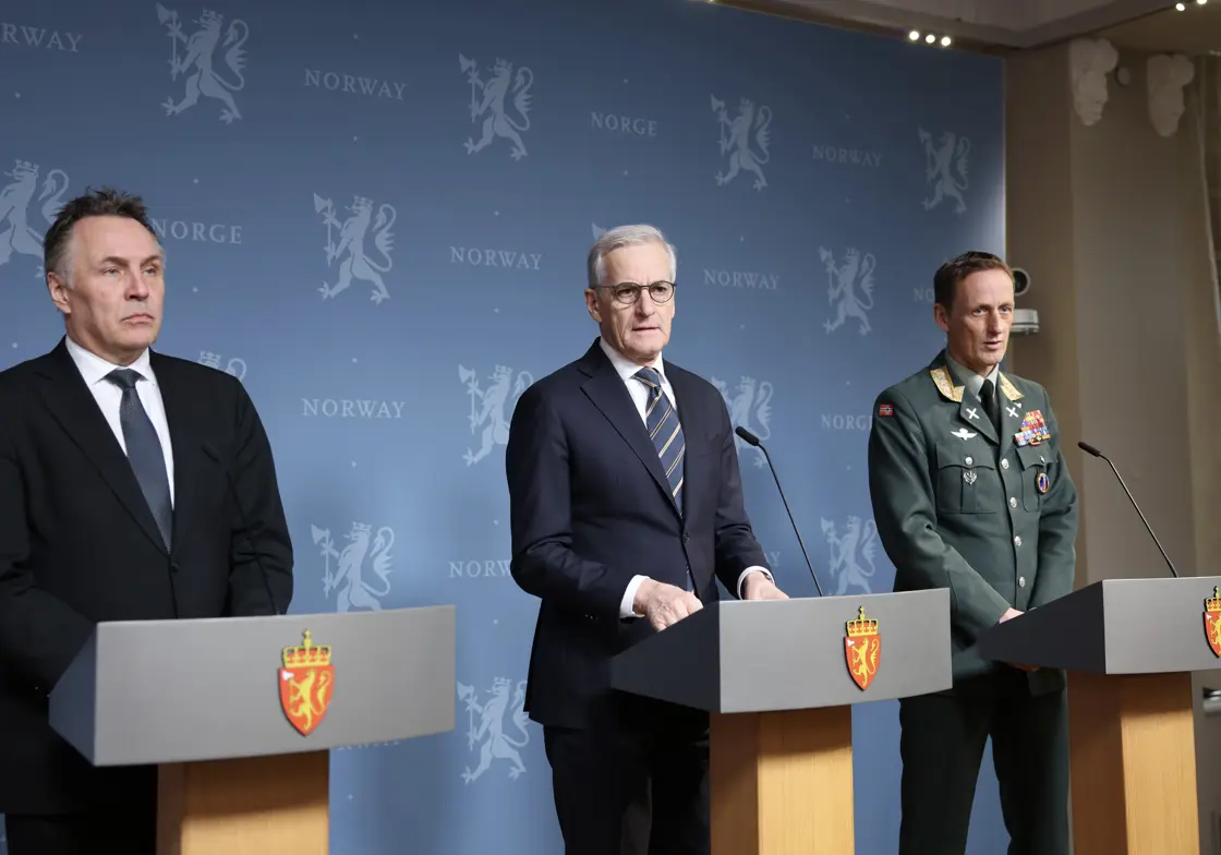 De tre står bak hver sin talerstol foran en blå vegg med riksløver.