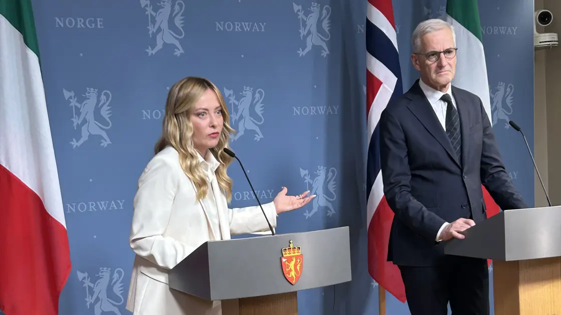 Pressekonferanse med Meloni og Støre. De står bak hver sin talerstol mot en blå bakvegg.