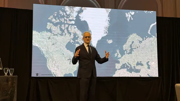 Statsministeren står på en scene foran et kart over nordområdene.