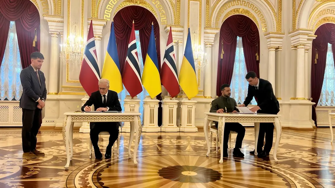 Statsministeren og presidenten sitter ved hvert sitt bord og signerer en avtale. Flagg i bakgrunnen.