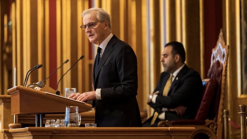 Statsministeren bak talerstolen på Stortinget. Stortingspresidenten i bakgrunnen.