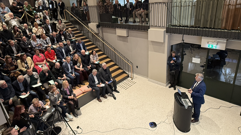 Kommunalminister Skjæran står i et auditorium. Bildet viser også deler av representantene fra byggenæringen som er til stede i salen. Sitter i et amfi.