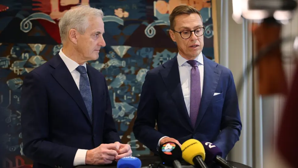 Støre og Stubb står ved siden av hverandre foran et veggteppe.