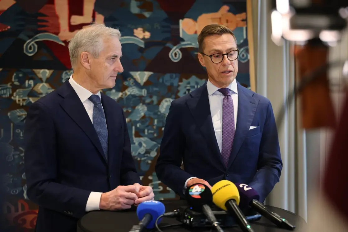 Støre og Stubb står ved siden av hverandre foran et veggteppe.