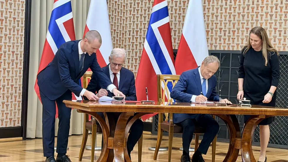 Støre og Tusk signerer avtalen. Begge sitter ved et stort bord.