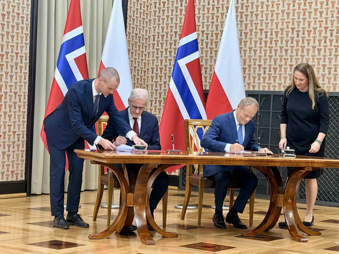 Støre og Tusk signerer avtalen. Begge sitter ved et stort bord.