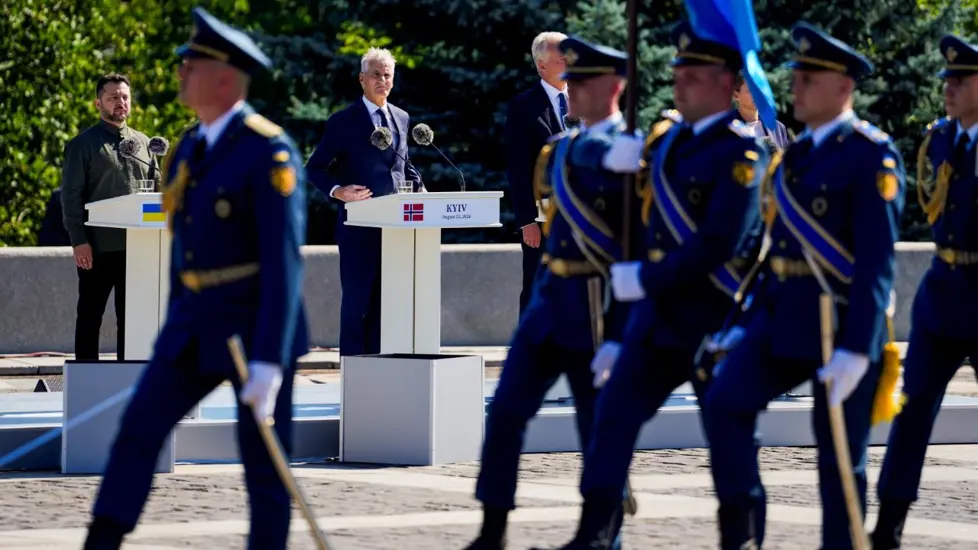 Støre og Zelenskyj ser på soldater som marsjerer med flagg foran talerstolene de står bak.