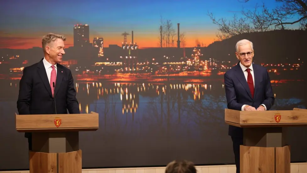 Støre og Aasland står på scenen foran en bakgrunn med bilde fra Herøya i Porsgrunn.
