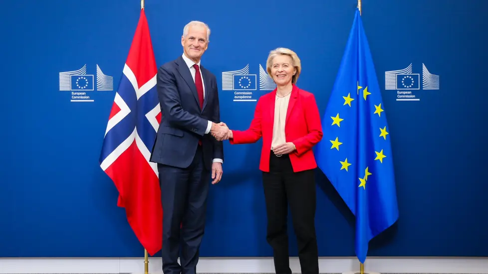 Statsministeren og EU-presidenten håndhilser foran flagg fra Norge og EU.