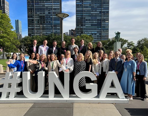 Bilde av gruppe mennesker oppstilt utendørs bak en skulptur med teksten #UNGA