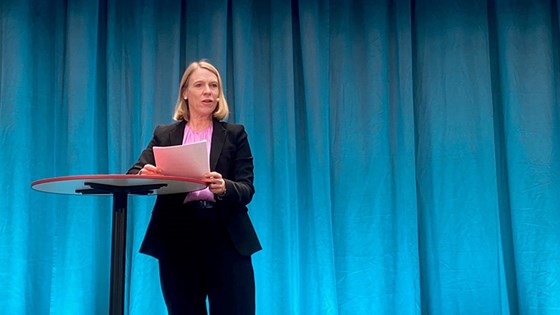 Bilde av utentiksminsiter Anniken Huitfeldt ved ståbord på scene med blå bakgrunn