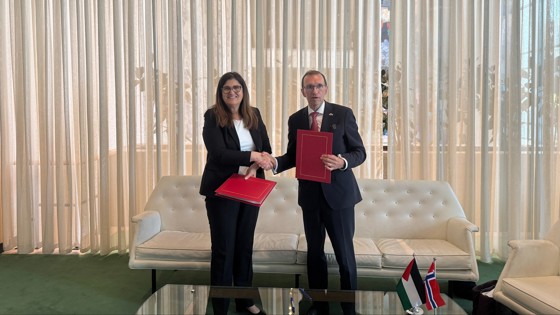 En mann og en kvinne med røde mapper i hendene fremfor et stort vindu