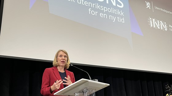 Bilde av utenriksminister Huitfeldt på talerstol med lerret i bakgrunnen. 