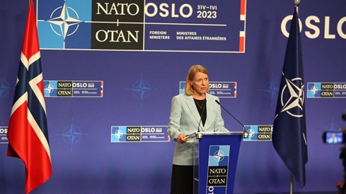 Picture of Foreign Minister Anniken Huitfeldt's at press conference with blue backround and norwegian and NATO flags