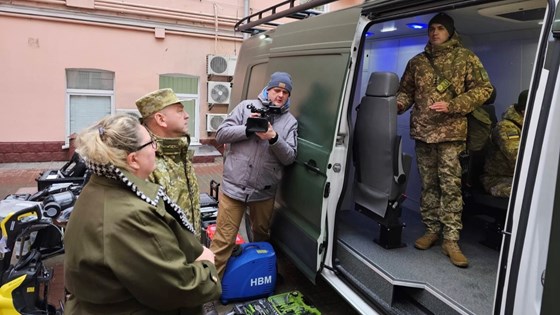 Norges ambassadør til Ukraina, Helene Sand Andresen står utenfor den grønne varebilen. En man i militæruniform står inni og forteller.