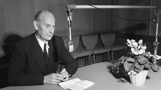 Statsminister Einar Gerhardsen sittende ved et bord med mikrofon.